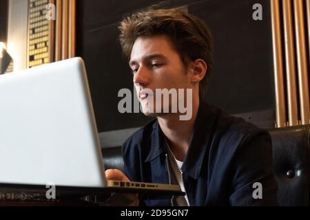 un giovane uomo si siede a un tavolo davanti a un computer portatile. un uomo che lavora su un computer portatile Foto Stock