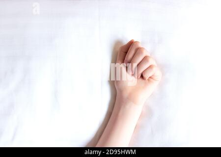 Bella mano femminile su biancheria da letto bianca al sole. Mano della donna su sfondo bianco. Messa a fuoco selettiva. Primo piano Foto Stock