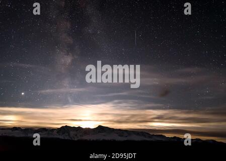 Incredibile paesaggio notturno con cielo stellato, galassia della Via Lattea, luna e belle nuvole all'orizzonte sopra le montagne innevate Foto Stock