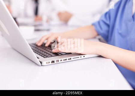 Primo piano dell'infermiere che scrive sul computer portatile durante l'incontro con i colleghi nella sala riunioni dell'ospedale. Terapeuta clinica esperta che parla con i colleghi di malattia, medico Foto Stock