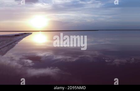 Bella alba su un lago rosa vicino ad una piccola isola, il riflesso del cielo blu sull'acqua, il colore viola del mare. Foto Stock