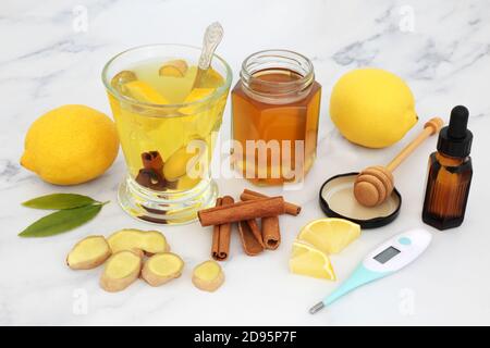 Cibo sano per il freddo, tosse e rimedio influenzale con termometro digitale, olio essenziale, bevanda calda di miele, limone, zenzero e spezie cannella su marmo. Foto Stock