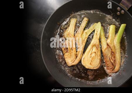 Arrostire le fette di finocchio in burro marrone in una padella di cottura su una stufa nera, preparazione per un pasto vegetariano, spazio copia, vista dall'alto, il concentrato selezionato Foto Stock