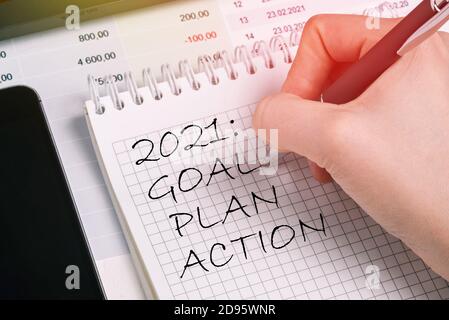 Il lavoratore di ufficio scrive un elenco per 2021 in un notebook. Concetto di pianificazione, impostazione degli obiettivi Foto Stock