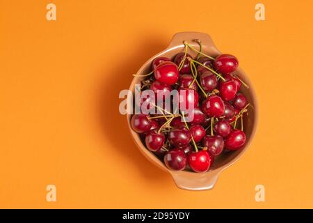 Ciliegie con gocce d'acqua in ciotola di argilla su sfondo terracota. Ciotola di frutta. Vista dall'alto. Cibo delizioso. Spazio di copia. Foto di primo piano di alta qualità. Foto Stock
