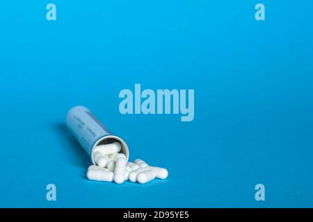 Un flacone con un mazzo di capsule bianche di compresse su sfondo blu. Foto Stock