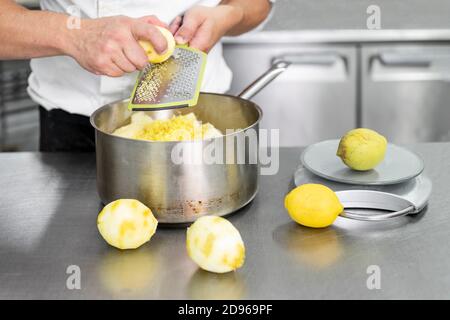 Una mano dello chef Pasticceria grattuce il limone in cucina commerciale.  Lo chef grates si lime sulla grattugia per ottenere la scorza per cucinare,  la preparazione di pasticceria, cibo sano Foto stock - Alamy