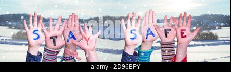 Bambini mani che tiene parola stare sicuro, Snowy sfondo invernale Foto Stock