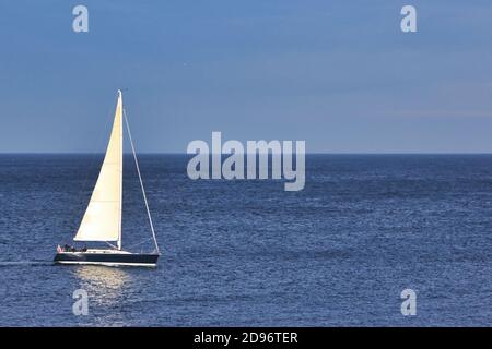 Barca a vela sul mare con un cielo blu chiaro e l'orizzonte sullo sfondo Foto Stock