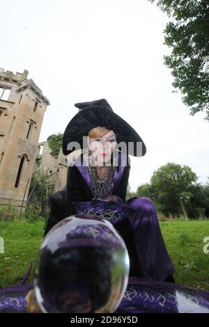 Donna anziana vestita come una strega con tarocchi carte & palla di cristallo all'esterno dell'edificio rovinato Foto Stock