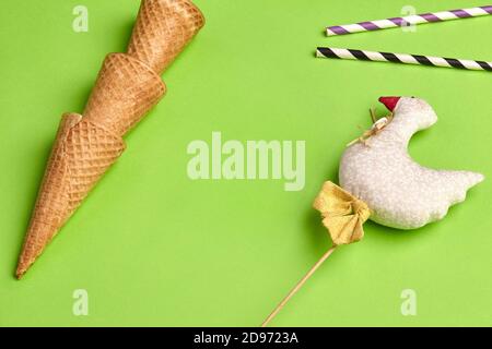 Tre cialde dolci vuote per gelato, due tubuli e anatra decorativa su bastone di legno su sfondo verde chiaro. Primo piano, spazio di copia Foto Stock