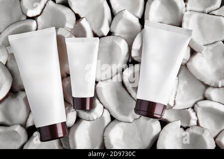 Tre tubi bianchi di diverse dimensioni senza logo o etichetta su pezzi o parti di sfondo di cocco. Confezionamento cosmetico, contenitori. Primo piano, spazio di copia Foto Stock