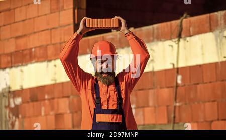 Mattone leggero fatto da aggregato di creta espanso. Elemento in muratura. Costruisca il mattone di tenuta. L'uomo con bearded indossa un cappello duro nel cantiere. Materiale di costruzione di mattoni usato per fare le pareti. Foto Stock