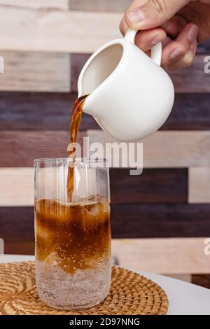 La mano dell'uomo versa l'espresso in un bicchiere con un tonico. Foto Stock