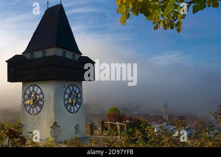 La famosa torre dell'orologio sulla collina di Schlossberg, a Graz, nella regione della Stiria, in Austria, all'alba. Bella mattina nebbia sulla città di Graz, in autunno Foto Stock