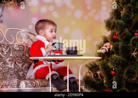 Un ragazzino in costume di Babbo Natale si siede a un tavolo bere tè Foto Stock