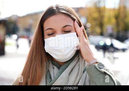 COVID-19 primo piano di giovane donna in città strada indossare la maschera chirurgica bianca soffre di mal di testa Foto Stock