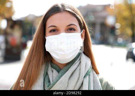 COVID-19 primo piano di giovane donna in città strada indossare maschera chirurgica bianca guardando la fotocamera. Ragazza con maschera protettiva sul viso contro Coronavirus D Foto Stock