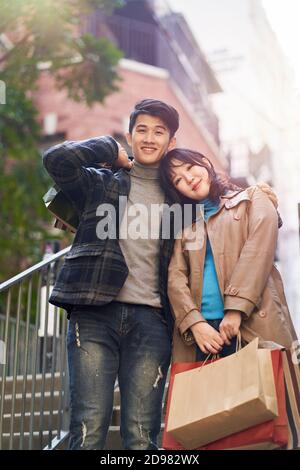 ritratto all'aperto di una giovane coppia asiatica felice di ritorno da una zona di shopping, guardando la macchina fotografica sorridente Foto Stock