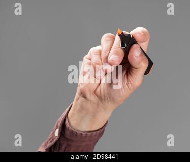 Una mano che tiene un marcatore arancione su sfondo grigio Foto Stock