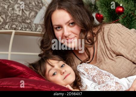 Mamma e figlia giacciono sui cuscini sotto l'albero di Natale Foto Stock