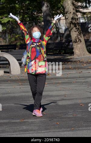 Una donna cinese americana di mezza età in una giacca colorata e sciarpa esercizi di danza con un gruppo in un parco a Flushing, Queens, New York City. Foto Stock