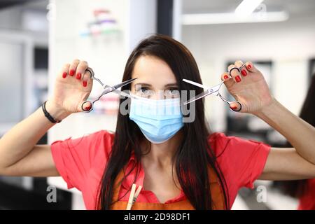 Parrucchiere in una maschera medica protettiva contiene forbici per tagliare i capelli. Foto Stock