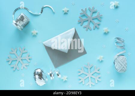 Cartolina di natale vuota e busta con decorazioni argentate su superficie blu, vista dall'alto. Spazio di lavoro hipster vacanze mock up, cartolina, layout festivo Foto Stock