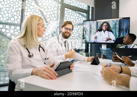 Team di medici multietnici, lezione di ascolto di dottore afro americano femminile alla videoconferenza medica in clinica. Focus su bello bearded Foto Stock