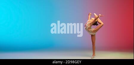 Volantino. Piccola ragazza caucasica, allenamento di ginnastica ritmica, che si esibisce isolato su sfondo gradiente blu-rosso in studio al neon. Aggraziato e flessibile, bambino forte. Concetto di sport, movimento, azione. Foto Stock