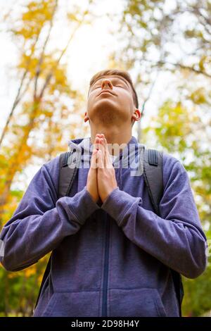 Il giovane uomo sta pregando solo nella foresta d'autunno Foto Stock