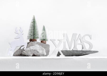 Xmas composizione moderna alla moda. Natale decorazioni bianche lettere XMAS, cervi, alberi di Natale su pietra si erge su bianco. Foto Stock