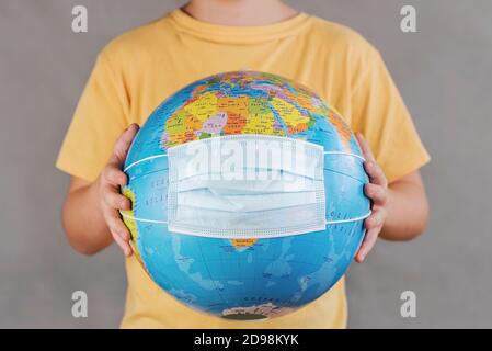 Coronavirus.Kid tenendo terra globo con maschera medica viso su grigio Background.Covid 19 concetto Foto Stock