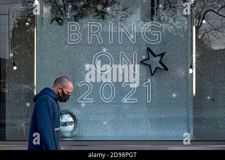 St Andrew Square, Edimburgo, 3 novembre 2020. L'uomo che indossa una maschera facciale passa accanto a un cartello nella finestra di Harvey Nichols che recita: 'Bring on 2021'. Foto Stock