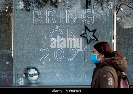 St Andrew Square, Edimburgo, 3 novembre 2020. Donna che indossa una maschera facciale cammina oltre un segno nella finestra di Harvey Nichols che recita: 'Bring on 2021'. Foto Stock