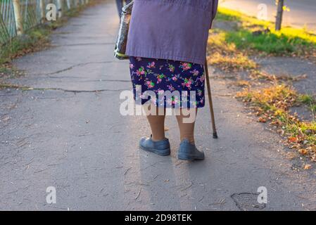 Nonna di circa settantacinque sulla strada con un bastone, limpe donna molto anziana con sciarpa testa seduta e rilassante in giardino Foto Stock