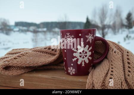 Coppa rossa o borgogna con un modello di fiocchi di neve sullo sfondo di una foresta invernale. Nevicare. Capodanno. Natale. Tazza con una bevanda calda sul Foto Stock