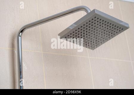Acqua che scorre dalla doccia in bagno con piastrelle beige sfondo. Interni semplici, eleganti e moderni. Primo piano Foto Stock