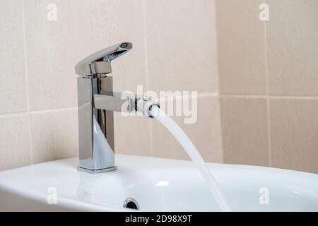 Dettagli di bidet in ceramica bianca con acqua corrente in bagno moderno con sfondo in piastrelle beige. Interni semplici ed eleganti e moderni Foto Stock