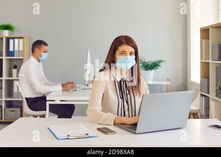 Giovani dipendenti in maschere mediche che lavorano su computer in l'ufficio aziendale Foto Stock