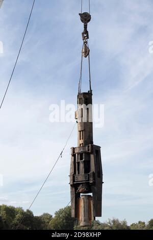 Gru da cantiere con gancio e grande punta industriale in acciaio appesa su funi che si sollevano, vista ad angolo basso con cielo nuvoloso Foto Stock