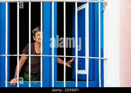 La vecchia donna cubana si affaccia attraverso i bar di una finestra all'esterno. Trinidad, Sancti Spíritus, Cuba, America Latina e Caraibi Foto Stock