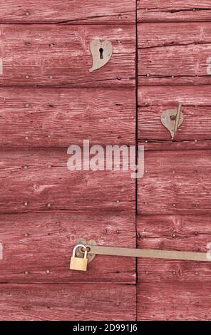 Primo piano di una vecchia porta esterna in legno di colore rosso con un impugnatura in ferro e due serrature Foto Stock
