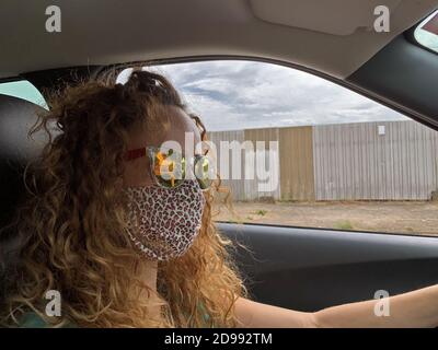 Donna con maschera protettiva in tessuto, guida la sua auto. Foto Stock