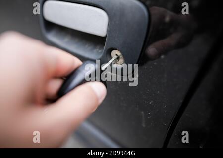 Immagine della profondità di campo poco profonda (messa a fuoco selettiva) con la mano di un uomo che apre un'auto di seconda mano con la chiave dell'auto. Foto Stock