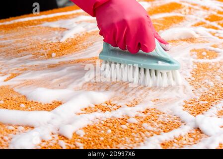 Donna Hand Cleaning Stain on Carpet con spazzola dura. Pulizia dei tappeti arancioni. Servizio di pulizia dei tappeti Foto Stock