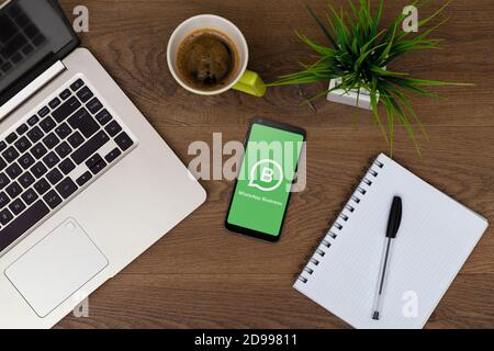 WhatsApp business sullo schermo del telefono. Vista dall'alto dell'area di lavoro. Scrivania con computer portatile, telefono cellulare, caffè, blocco note Foto Stock