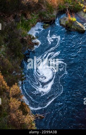 Schiuma superficiale spiralante dalla cascata dal torrente al serbatoio di Greenfield, sopra il lago artificiale dove Stone, vicino Oldham. Foto Stock