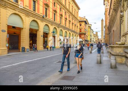 Bologna, Italia - 9 maggio 2020: Coppia con le maschere chirurgiche che camminano in via Ugo Bassi con due torri sullo sfondo. Coronavirus volte con Foto Stock