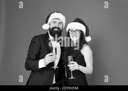 Festa di Natale. tuxedo uomo con la donna a santa hat. Buon Natale e saluti a tutti. business man e ragazza bere champagne. xmas party formali matura in amore festeggiare il nuovo anno. Foto Stock